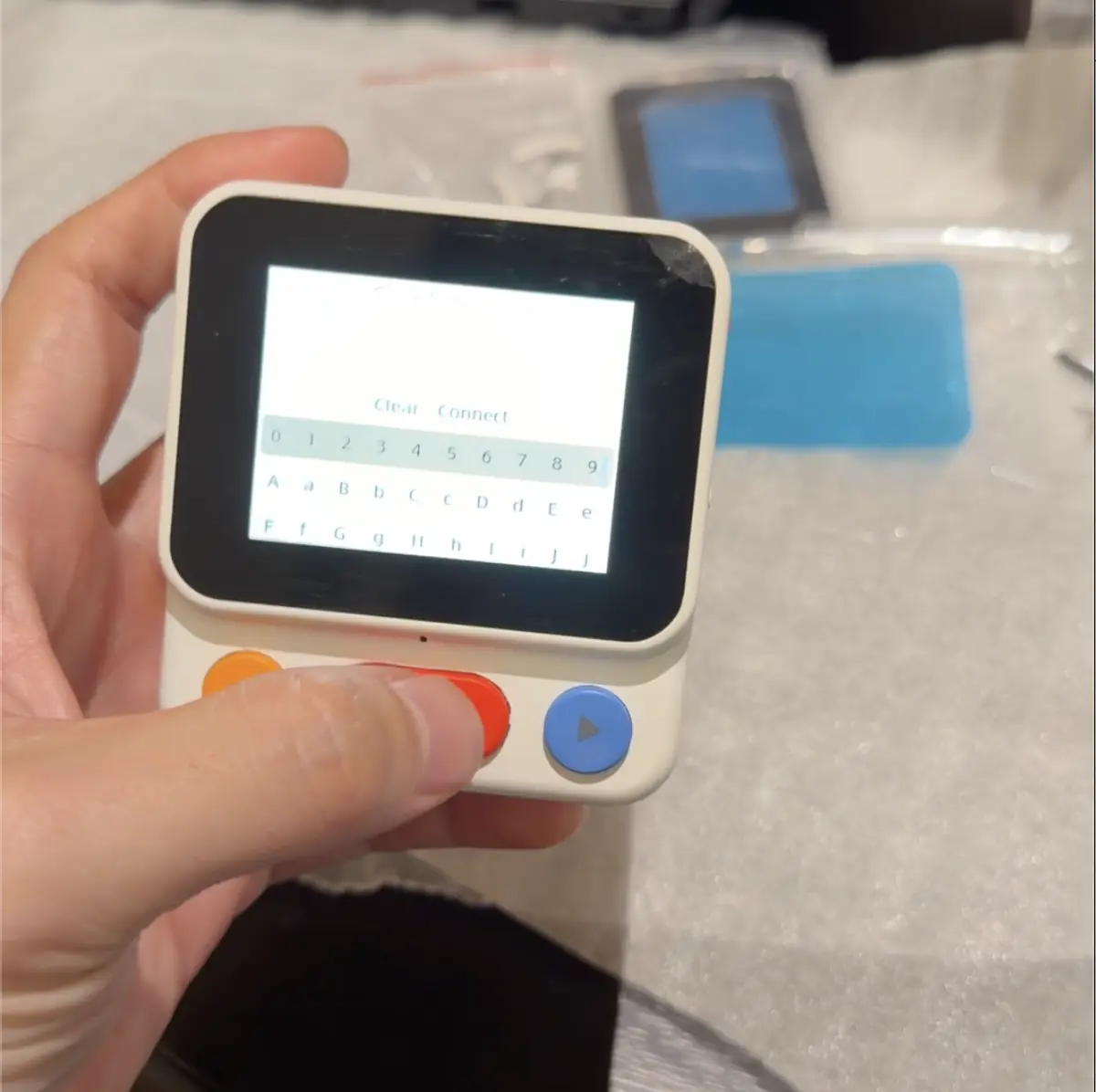 A working Nowa prototype held in one hand, screen and buttons live